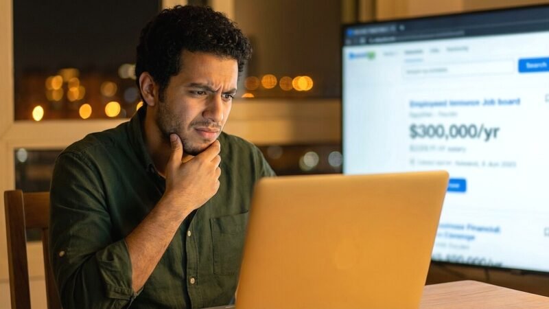 شاب مصري ينظر بشك لإعلان وظيفة وهمية على لابتوب في شقة بالقاهرة وتجنب شركات النصب الأونلاين.